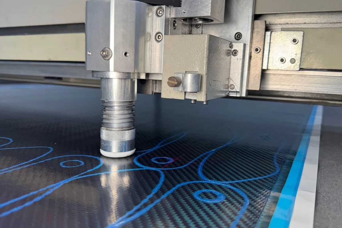 Carbon fabric on the cutting table with nested ply outlines projected across it