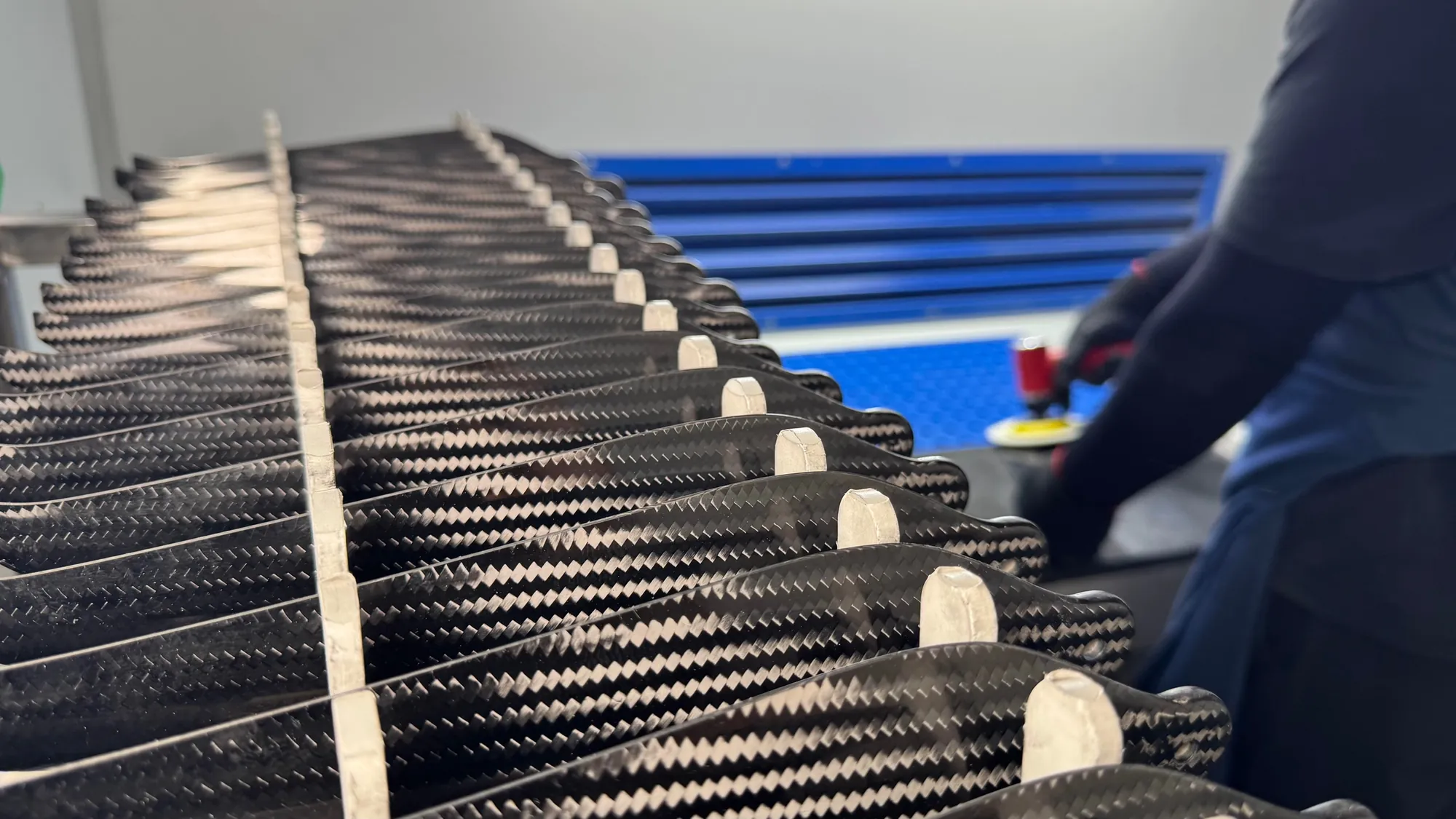 Finished blades racked in rows while an operator hand-finishes an edge